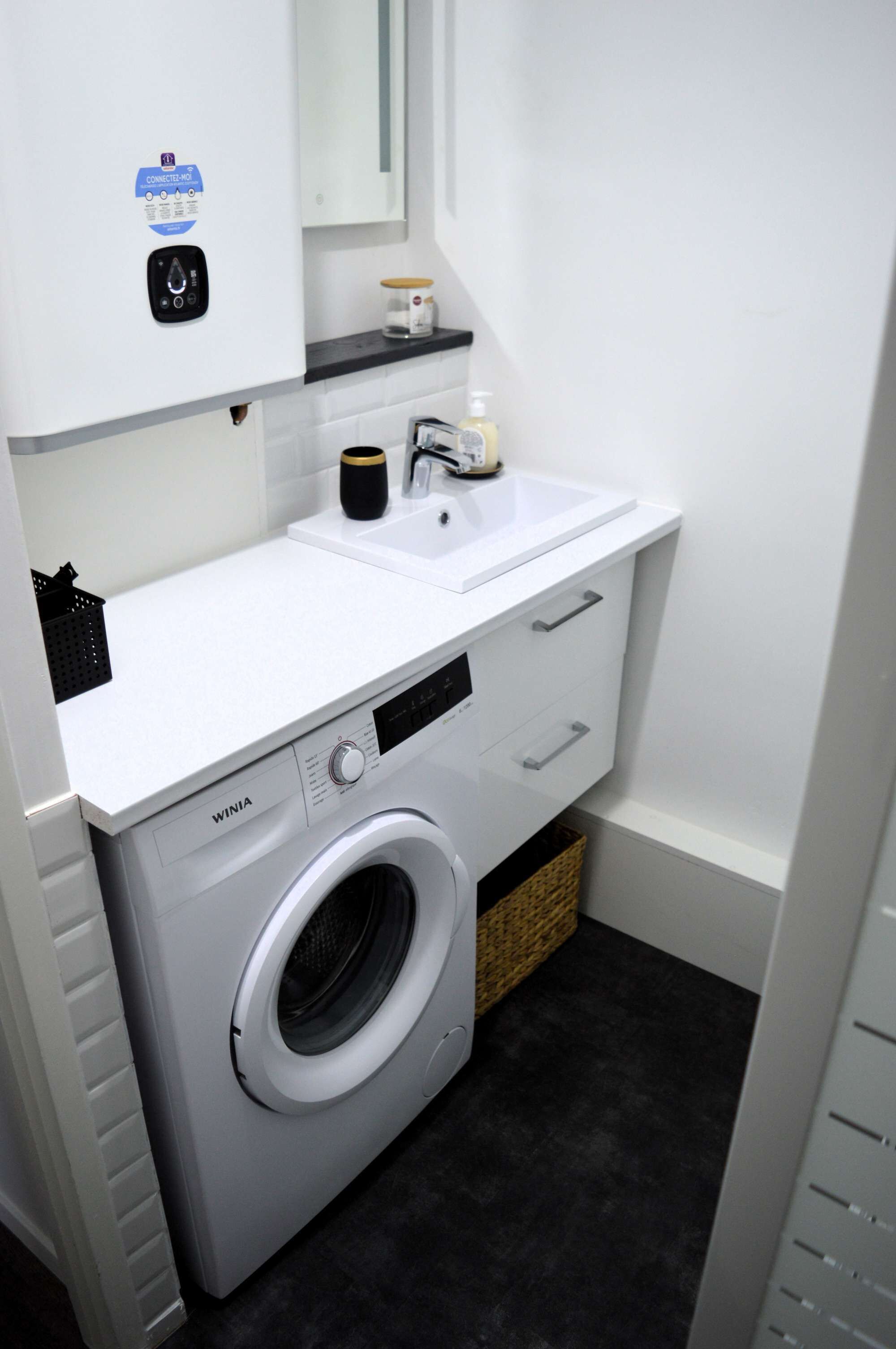 A compact laundry area with a front-loading washing machine, a sink, and a small countertop with a soap dispenser.