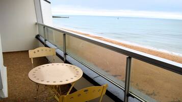 A balcony with a table and two chairs, overlooking a beach with a pier in the distance.