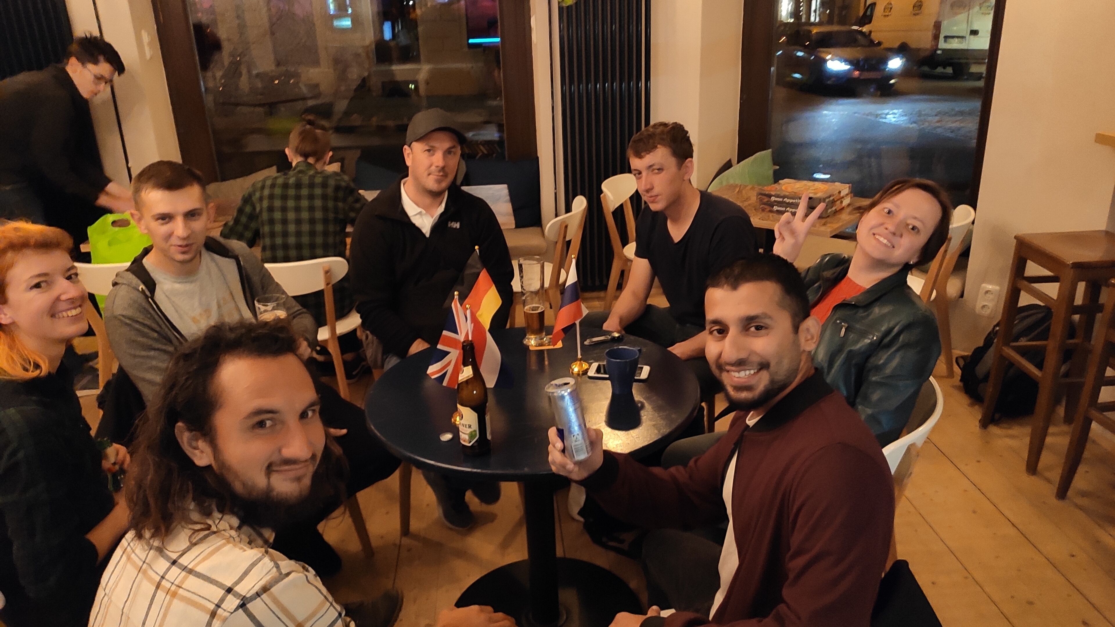 Un grupo de personas sentadas alrededor de una mesa redonda en un restaurante, con banderas, una botella y una lata de cerveza sobre la mesa.