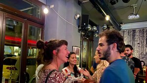 Un grup de persones en un espai interior amb poca llum, amb llums al sostre visibles i una finestra gran a l'esquerra.