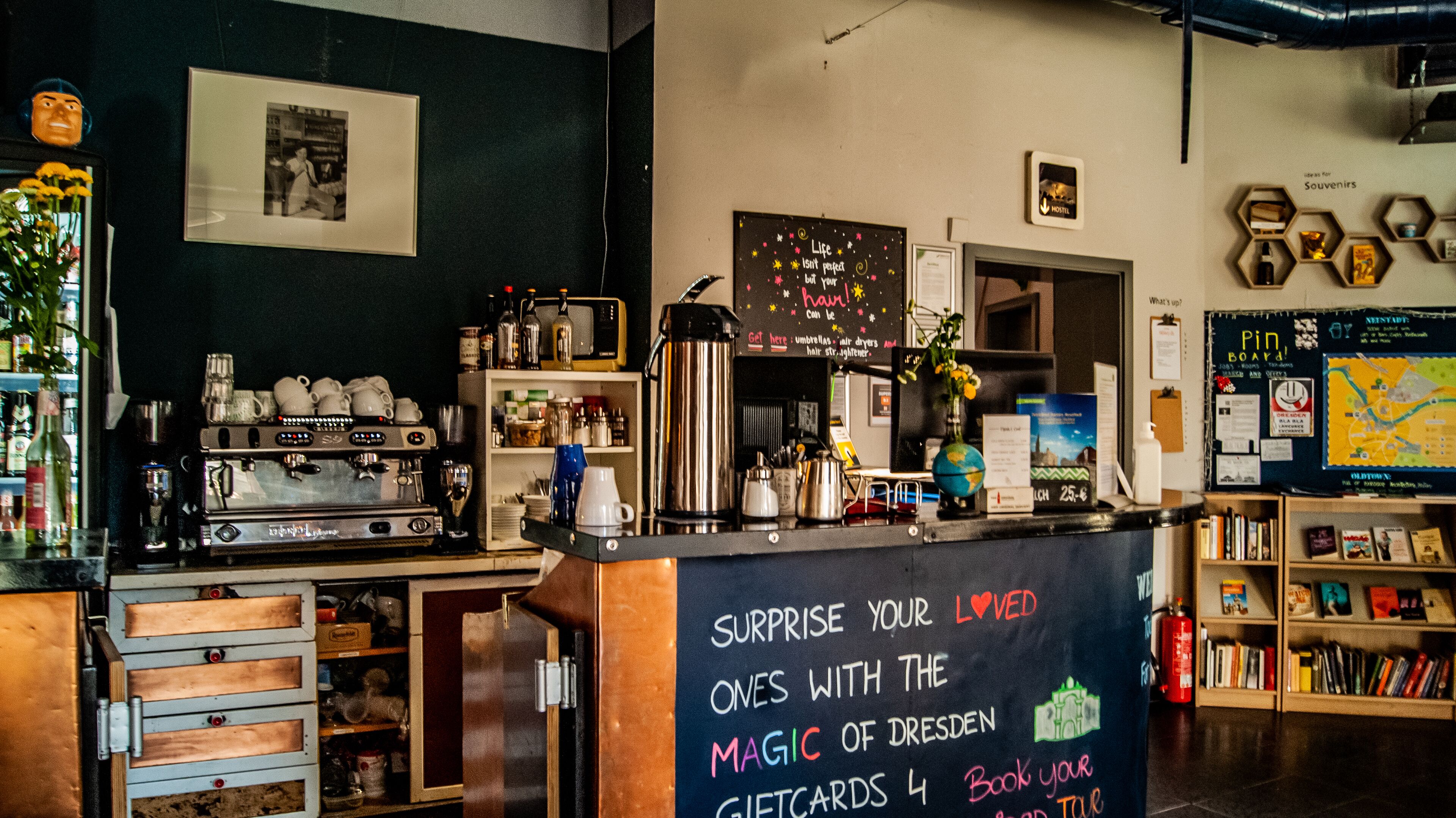 A coffee shop interior with a chalkboard sign, espresso machine, and shelves with various items.