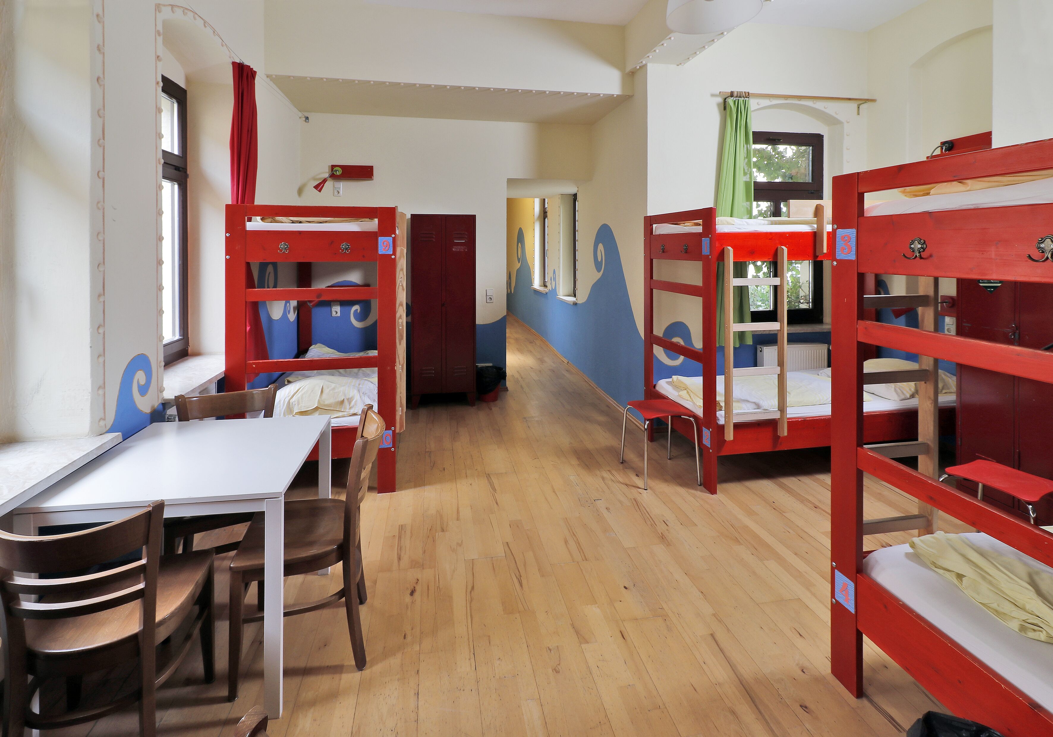 A dormitory room with bunk beds, a table, chairs, and a window.