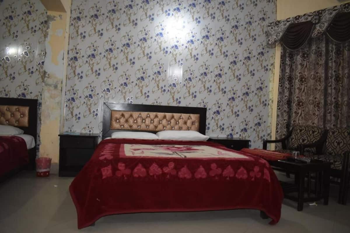 Ein Schlafzimmer mit zwei Betten, Blumenmuster-Tapete, einer roten Bettdecke und einem dunklen Holzstuhl.