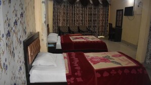 A hotel room with two beds, each with a red floral bedspread and white linens. There is a television on the wall and a desk with a chair.