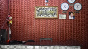 A reception area with a patterned red wall, a framed artwork, clocks displaying different cities, and a check-out time sign.