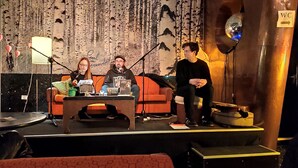 A stage with three people seated, a microphone stand, a table with items, and a backdrop with a forest pattern. - Doppelzimmer mit Bad (Dresden)