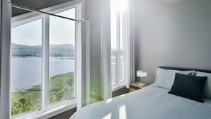 Ein Schlafzimmer mit einem großen Fenster und Blick auf einen See und Hügel.