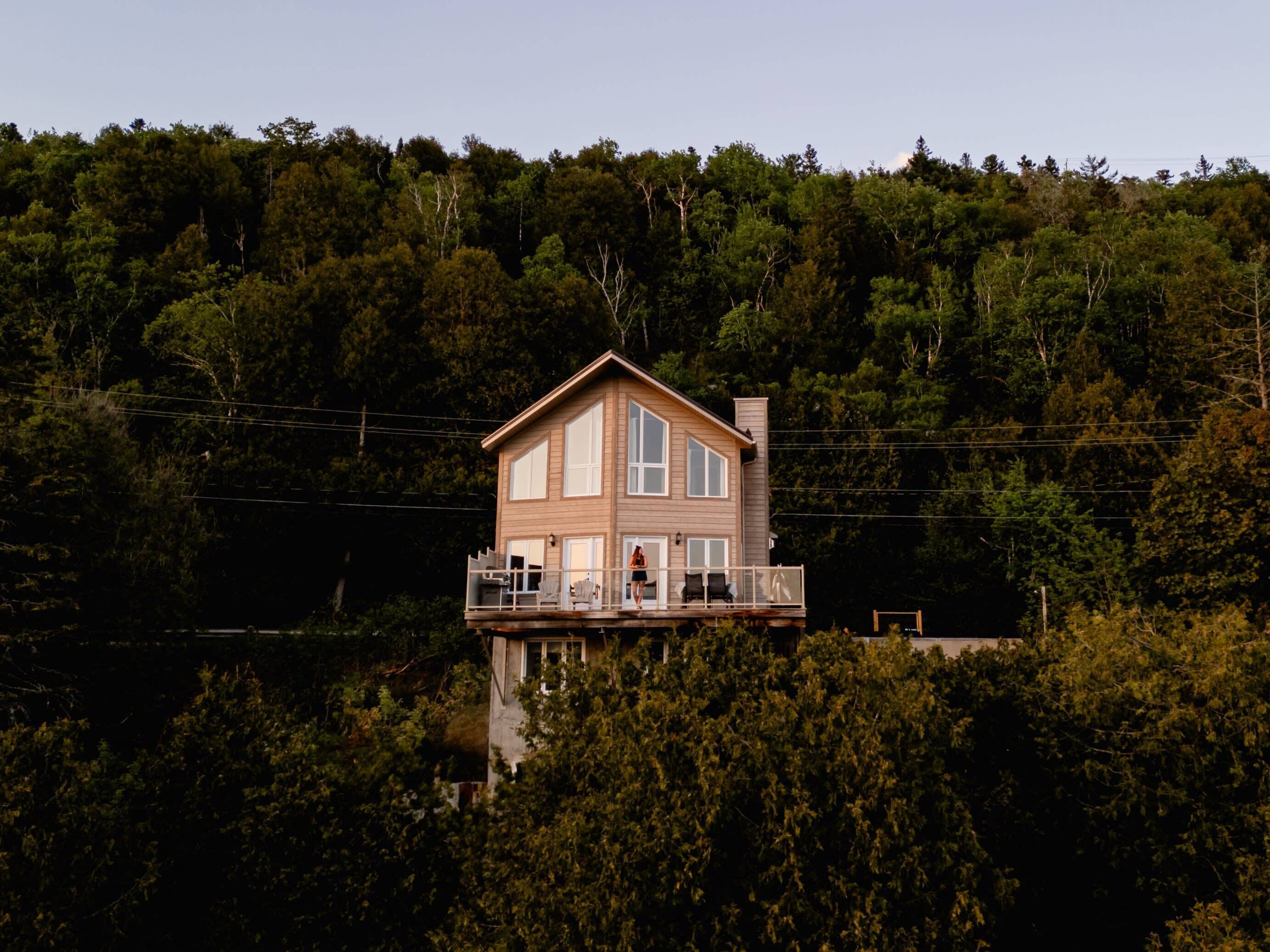 A two-story house with a balcony, surrounded by dense forest.