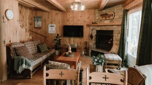 Ein gemütliches Blockhaus-Interieur mit Holzausstattung, Kamin, Fernseher und einer Couch.