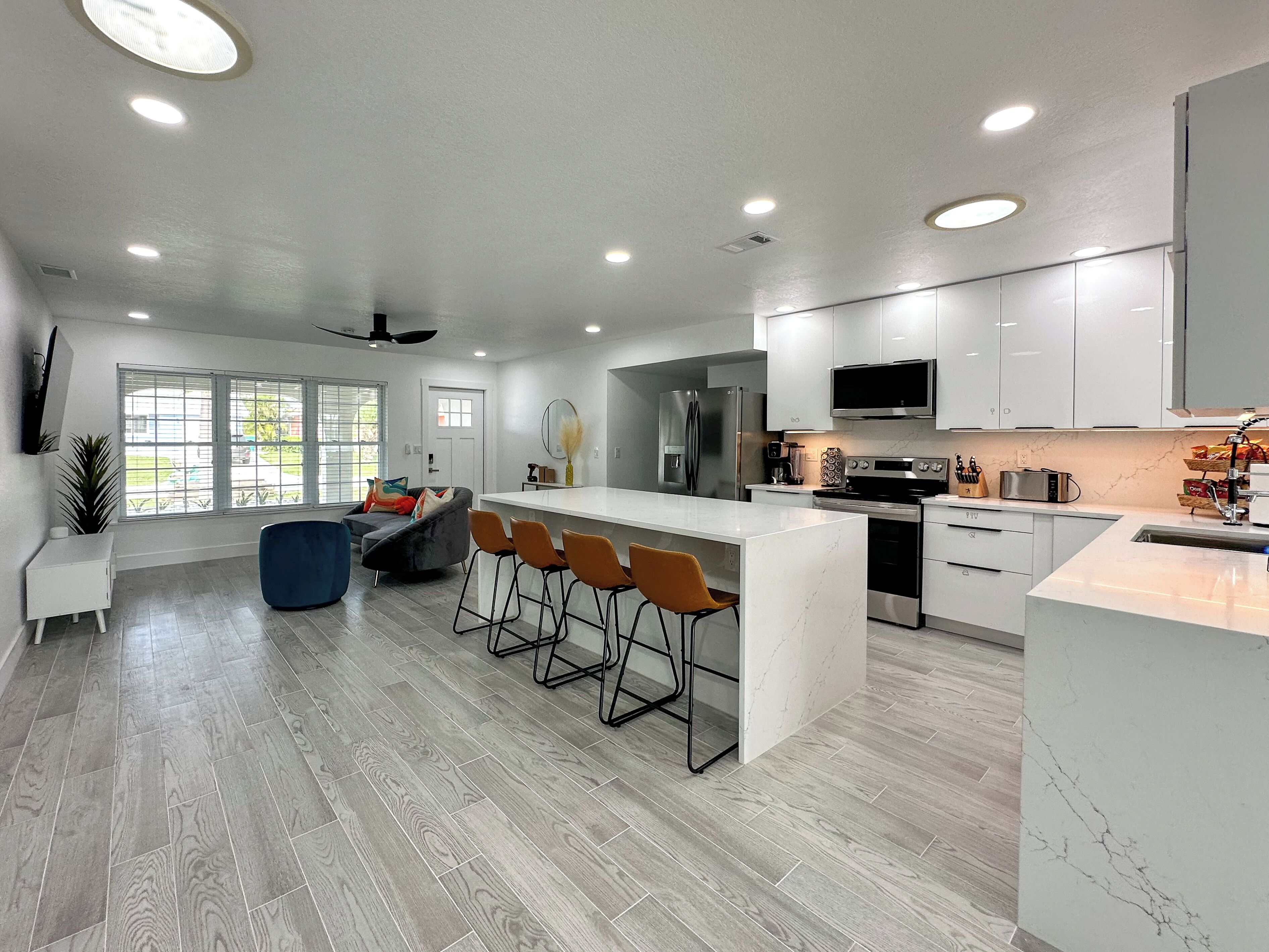 A modern kitchen with a central island, bar stools, a refrigerator, microwave, oven, and a large window.