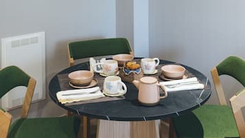 Un comedor con una mesa redonda, sillas tapizadas en verde y una encimera de mármol negro. Se observan obras de arte enmarcadas en las paredes y un radiador debajo de la mesa.