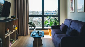 Una sala de estar con un ventanal amplio, un televisor, un sofá y una pequeña mesa con una planta.