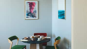 Un comedor con una mesa redonda, dos sillas verdes y dos obras de arte enmarcadas en la pared.