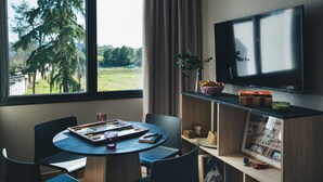 Una habitación con una mesa redonda, sillas, un televisor y una ventana que da a vistas de árboles.