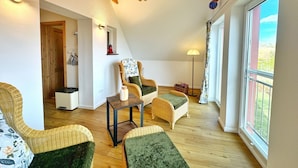 Een knus loft-achtig vertrek met hoge plafonds, zichtbare houten balken en een groot raam met uitzicht op de omgeving.