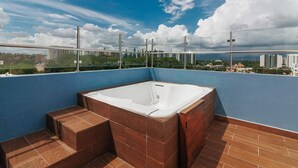 Una terraza en la azotea con jacuzzi, piso de madera y vistas panorámicas de la ciudad.