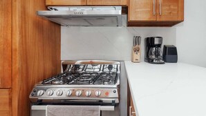 Una cocina con estufa a gas, armarios de madera, campana extractora de acero inoxidable y cafetera.