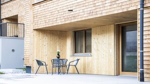 A modern building with a wooden facade, a balcony, and a patio area with a table and chairs. - HUUS123, Apartment 3 (Au)