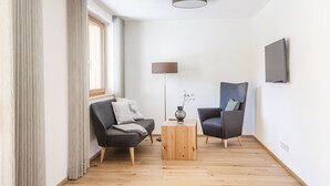 A modern living room with a sofa, armchair, and coffee table, a flat-screen TV mounted on the wall, and a window with curtains. - HUUS123, Apartment 3 (Au)