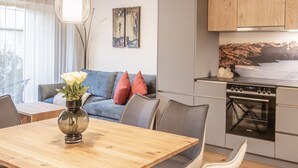 A modern kitchen with a built-in oven and microwave, a dining area with a wooden table and chairs, and a living area with a sofa and cushions. - HUUS123, Apartment 4 (Au)