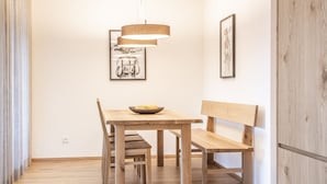 Une table à manger en bois avec des bancs, un saladier rempli de fruits et deux œuvres d’art encadrées accrochées au mur.