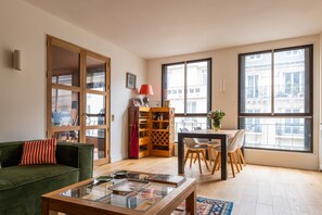 A living room with a sofa, coffee table, and a dining area with chairs and a table. - Footsteps From Trocadéro, by Veeve (Paris)