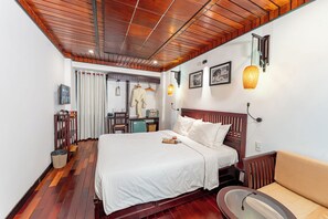 A hotel room with a wooden ceiling, a bed with white bedding, a wooden nightstand, a beige sofa, and a small table with a lamp. - Annam Heritage Boutique Hotel & Spa (Da Nang)