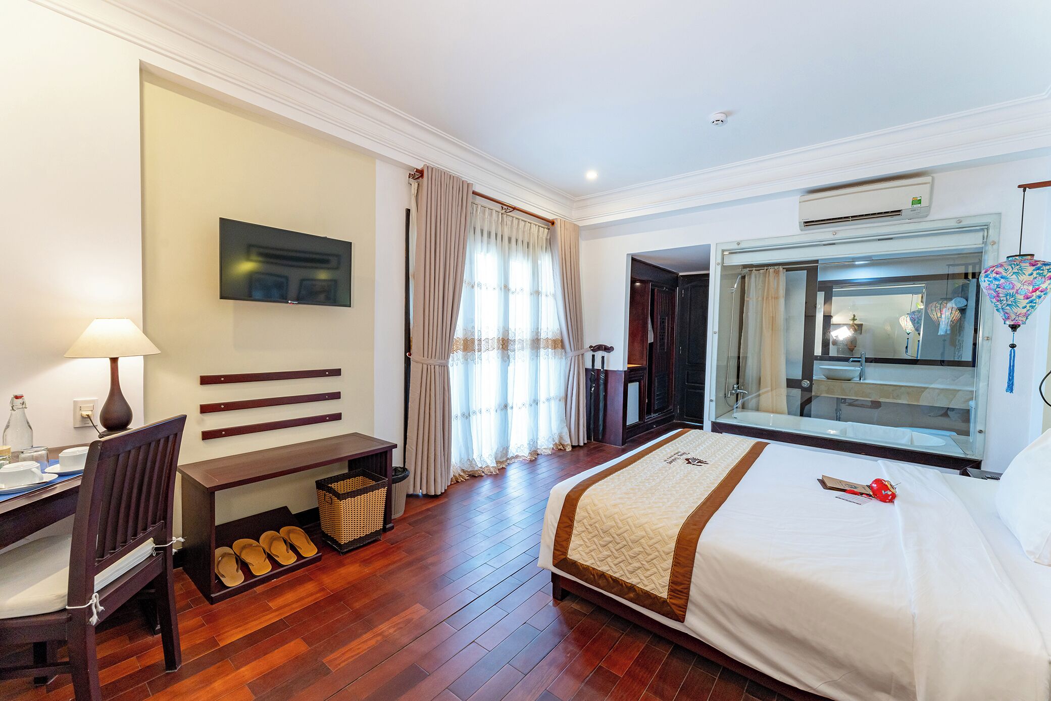 A hotel room with a bed, desk, chair, and a large window with curtains.