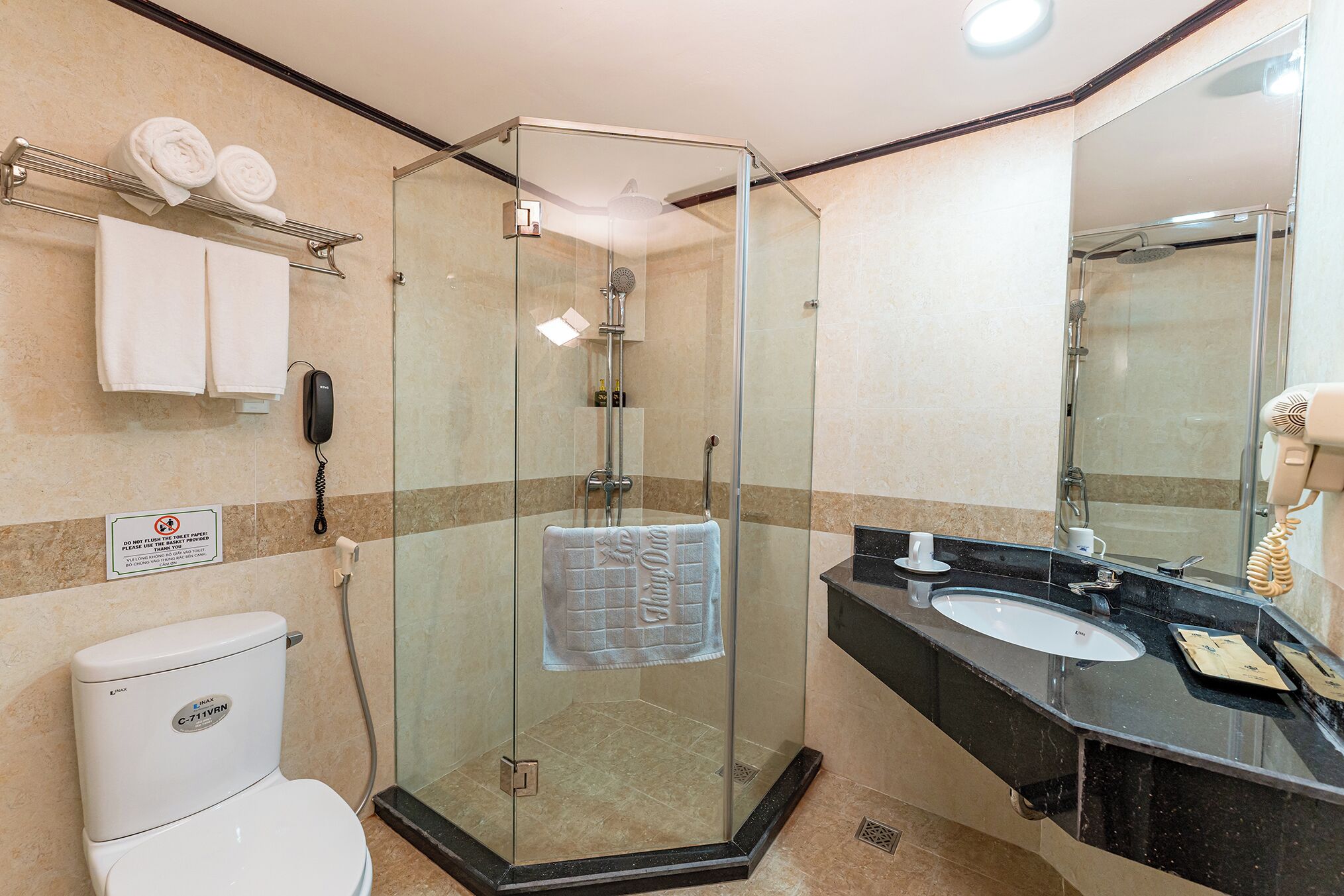 A modern bathroom with a glass-enclosed shower, a white toilet, a black sink, and a mirror.