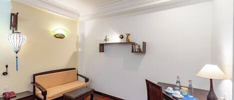 A room with a sofa, a small table, a dining table with chairs, a lamp, and wall-mounted shelves with decorative items.