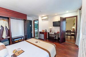 Habitación de hotel con cama, escritorio, televisor y baño visible a través de una puerta abierta.