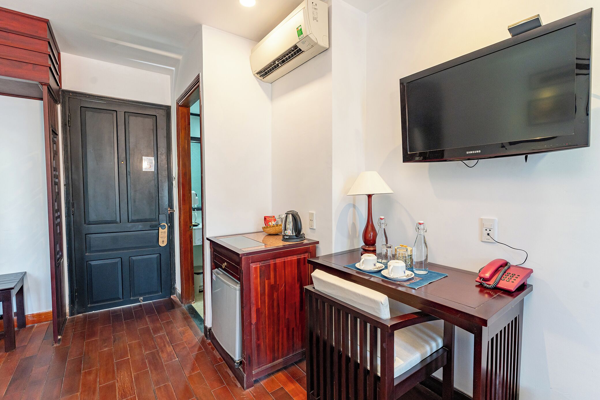 Una habitación de hotel con un escritorio de madera, televisor, teléfono y minibar.