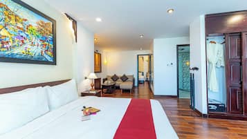 Habitació d'hotel amb un llit gran, un corredor vermell, un quadre a la paret, un armari de fusta i un bany visible a través d'una porta oberta.