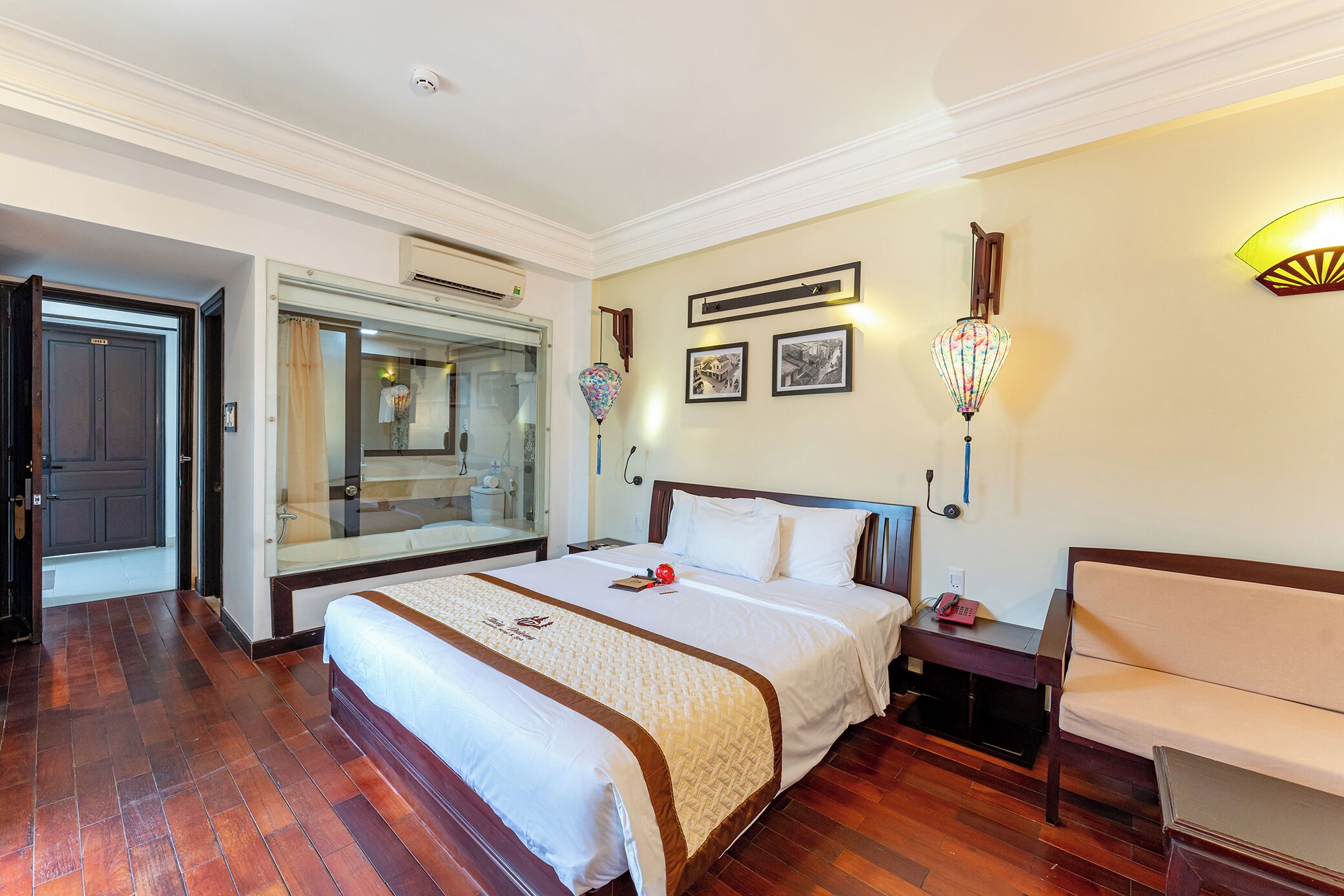 A hotel room with a large bed, a bedside table with a lamp, a chair, and a mirror.
