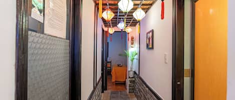A hallway with a stone floor, a wooden door on the right, and a table with a yellow tablecloth in the distance.