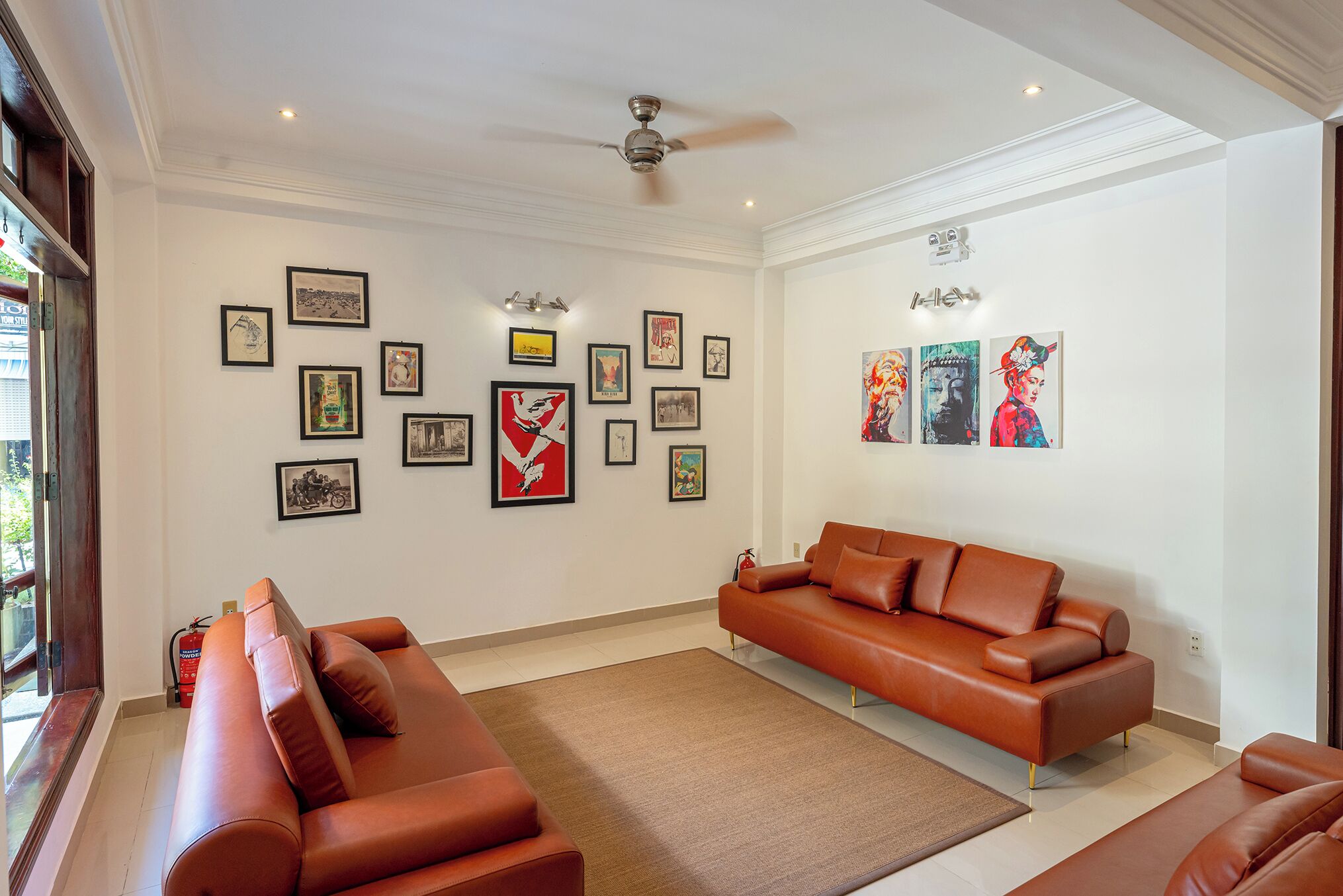 A modern living room with a brown leather sofa, a coffee table, and a ceiling fan. The walls are adorned with framed artwork.