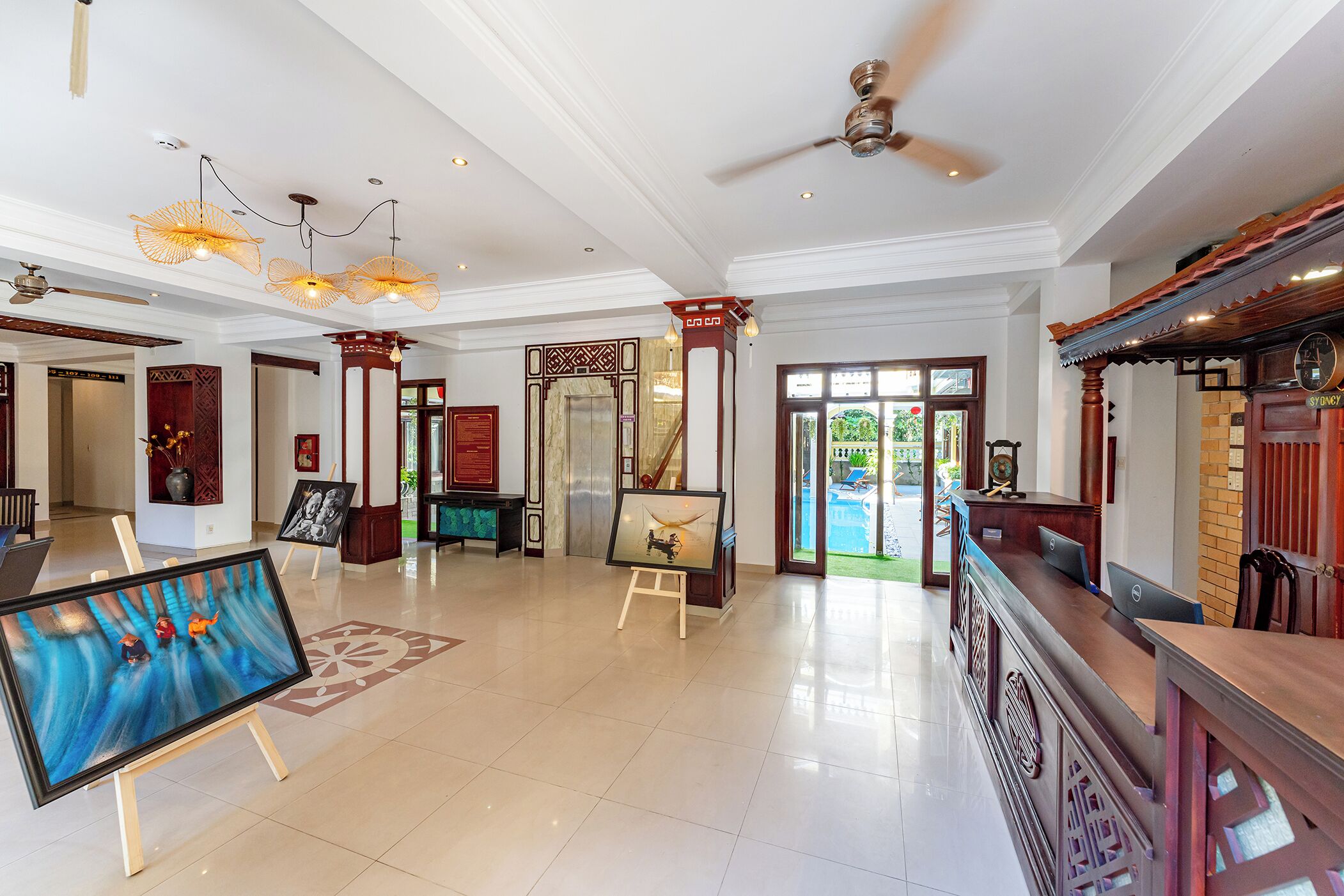 A spacious lobby with a reception desk, artwork on easels, and a ceiling fan.