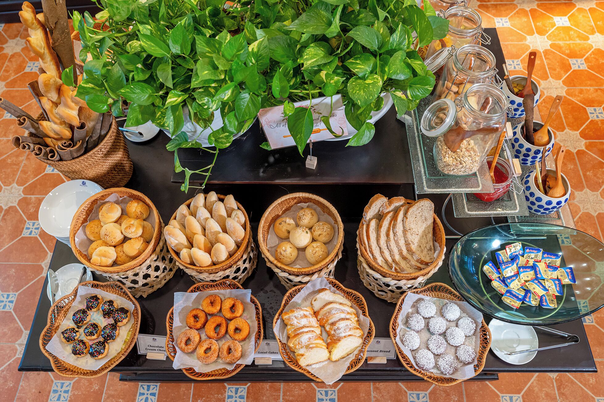 A buffet table with various baked goods, including bread, pastries, and cookies, arranged in baskets and on a glass display.