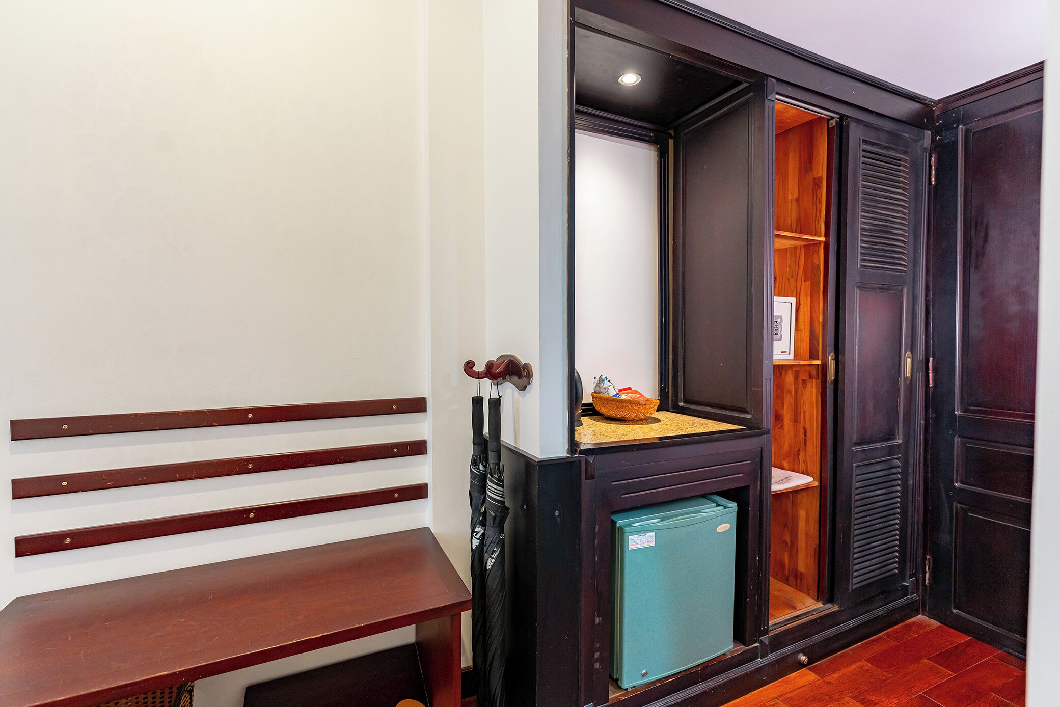 A room with a wooden bench, a small refrigerator, and a mirror.