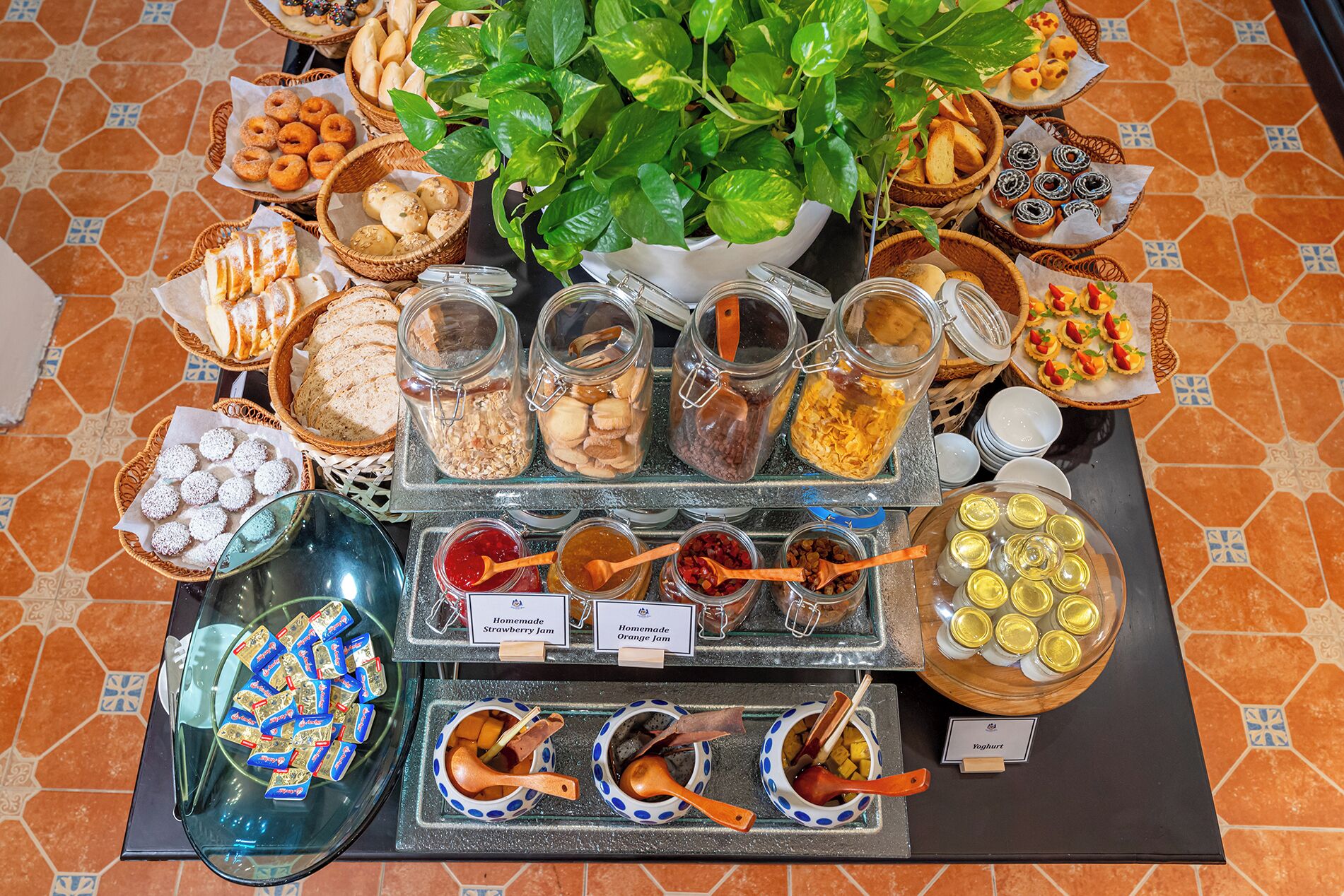 Une table de buffet proposant divers aliments, notamment des pots de confitures, des pâtisseries et un bol de yaourt.