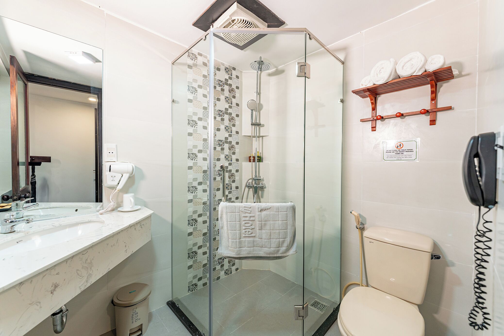 A modern bathroom with a glass-enclosed shower, a toilet, a sink with a mirror, and a towel rack with towels.