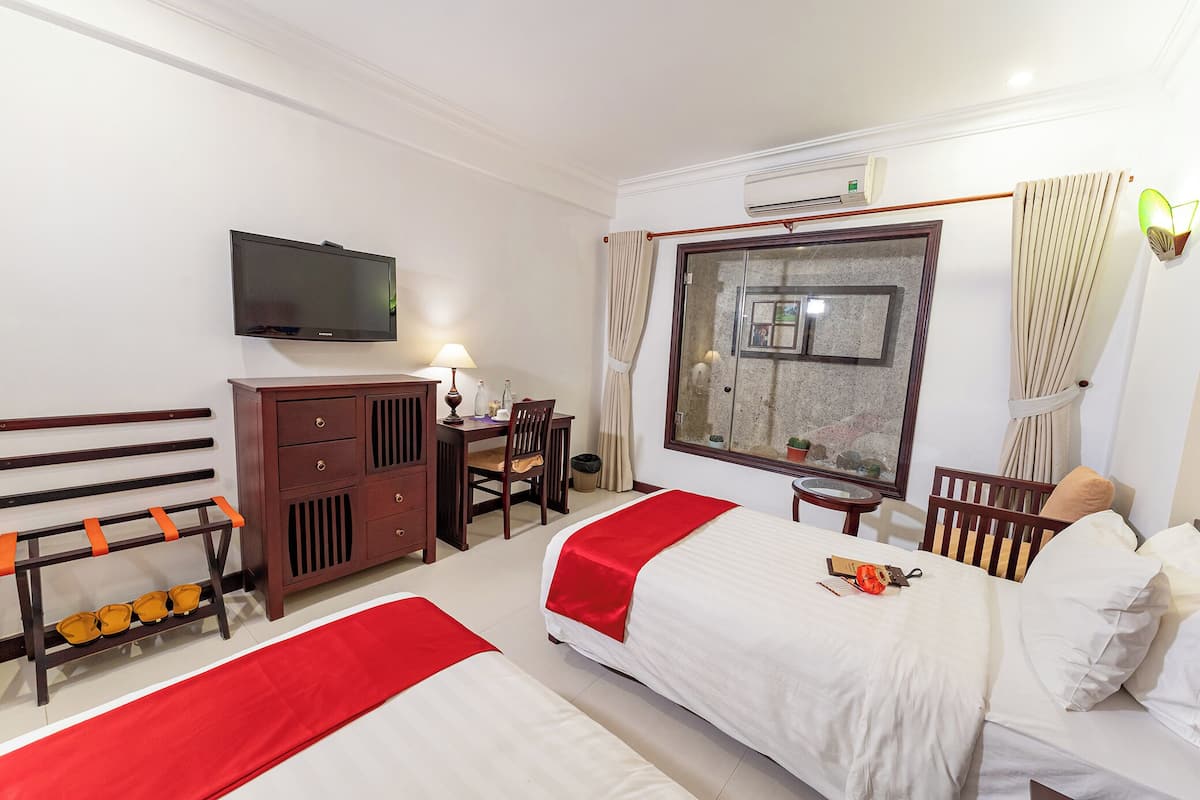 Ein Hotelzimmer mit zwei Betten, einem Schreibtisch, einem Stuhl, einem Fernseher und einem Fenster mit Vorhängen.