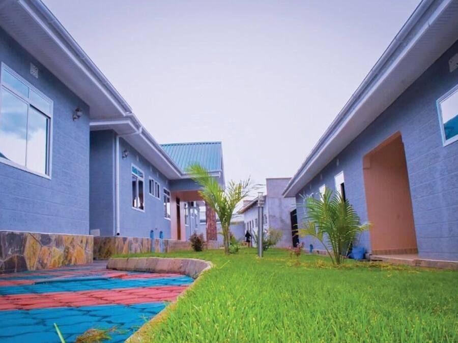 Un edificio moderno con fachada azul, un patio empedrado con baldosas de colores y un césped cuidado.
