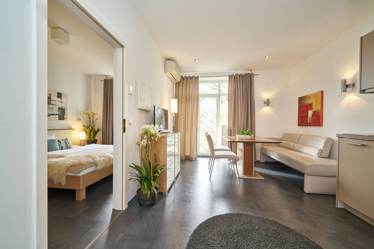 A modern hotel room with a bed, a desk, a sofa, and a dining area.