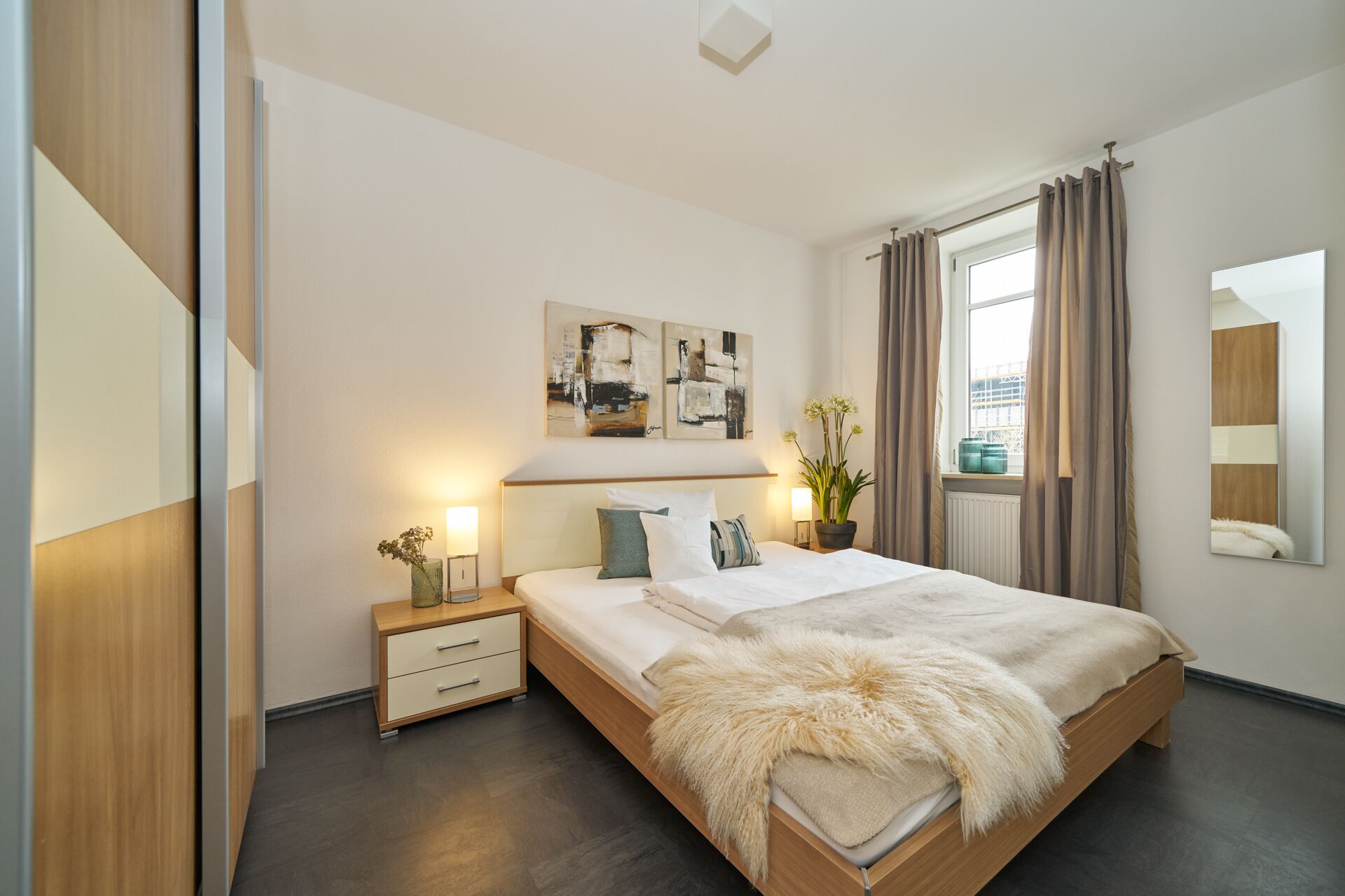 A modern bedroom with a large bed, bedside tables, a mirror, and artwork on the wall.