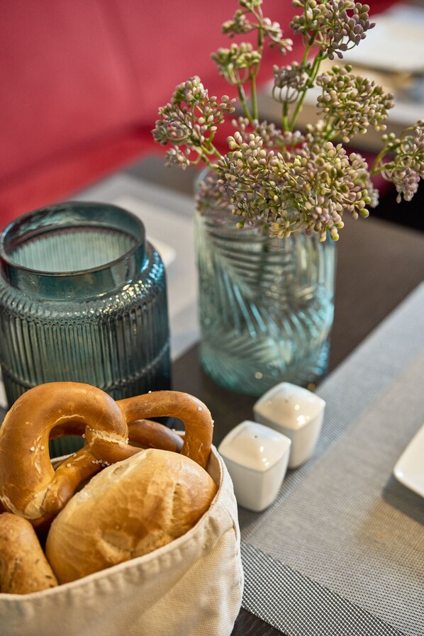 A table with a basket of pretzels, a jar of flowers, and a salt and pepper shaker. - Hotel am Hof (Taufkirchen)