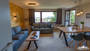 Un salon moderne avec un canapé, une table basse et une table à manger. Il y a une fenêtre avec des rideaux, une lampe et une vue sur l’extérieur.