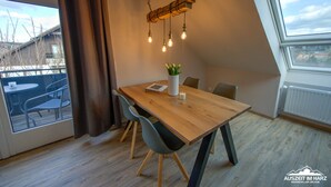 A dining area with a wooden table, four chairs, a vase with flowers, and a hanging light fixture.