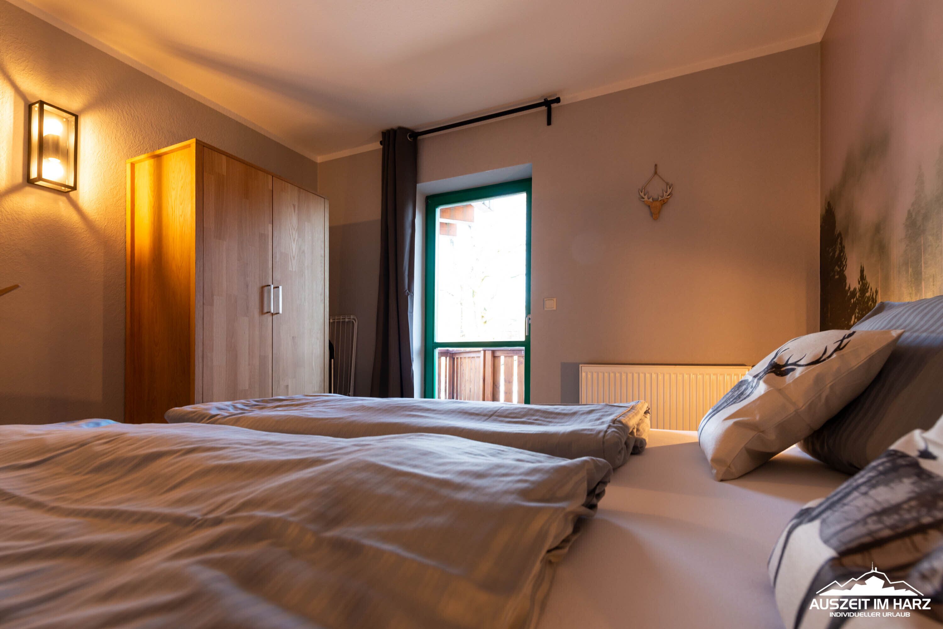 A bedroom with two beds, a wardrobe, a window with curtains, and a wall-mounted light fixture.