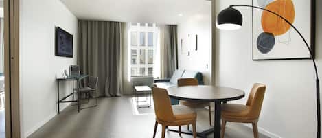 A modern living room with a dining area, a sofa, a coffee table, and a large window with curtains.